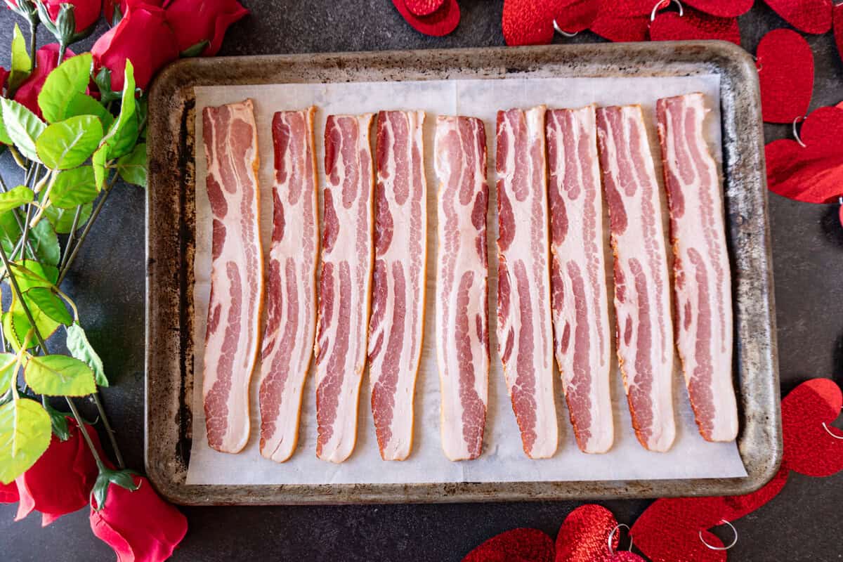 uncooked slices of bacon on baking sheet.