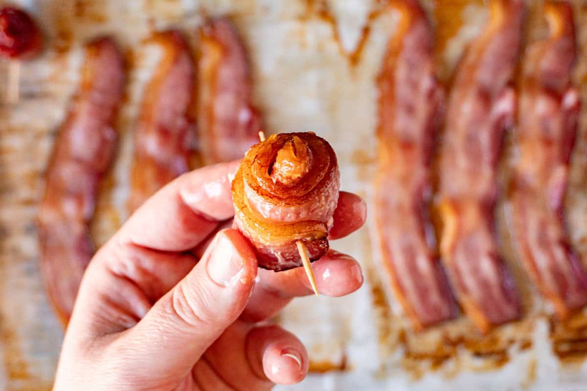 holding a rolled piece of bacon with a toothpick through it.