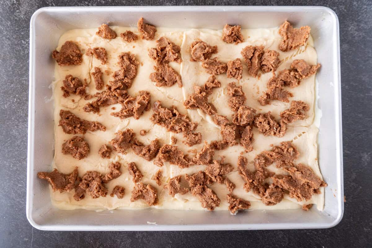 cinnamon topping dotted onto crescent roll in baking dish.