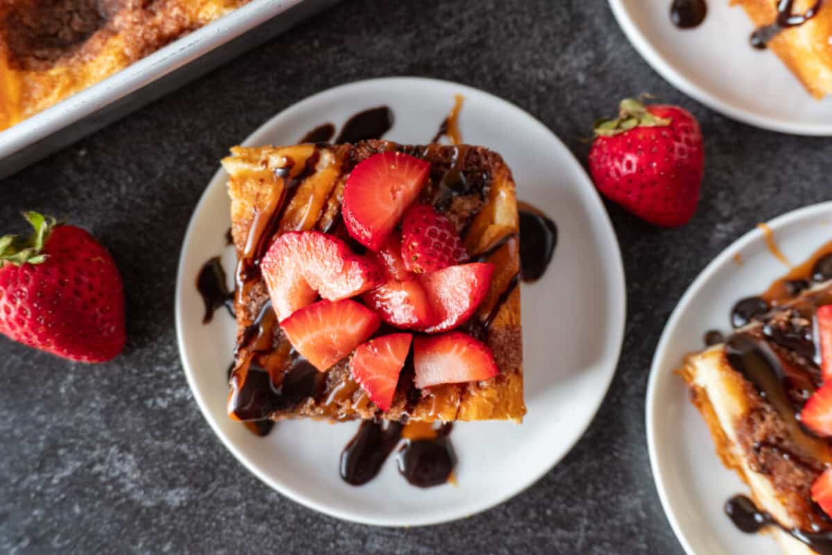 churro cheesecake topped with strawberries, caramel, and chocolate sauce on a white plate.