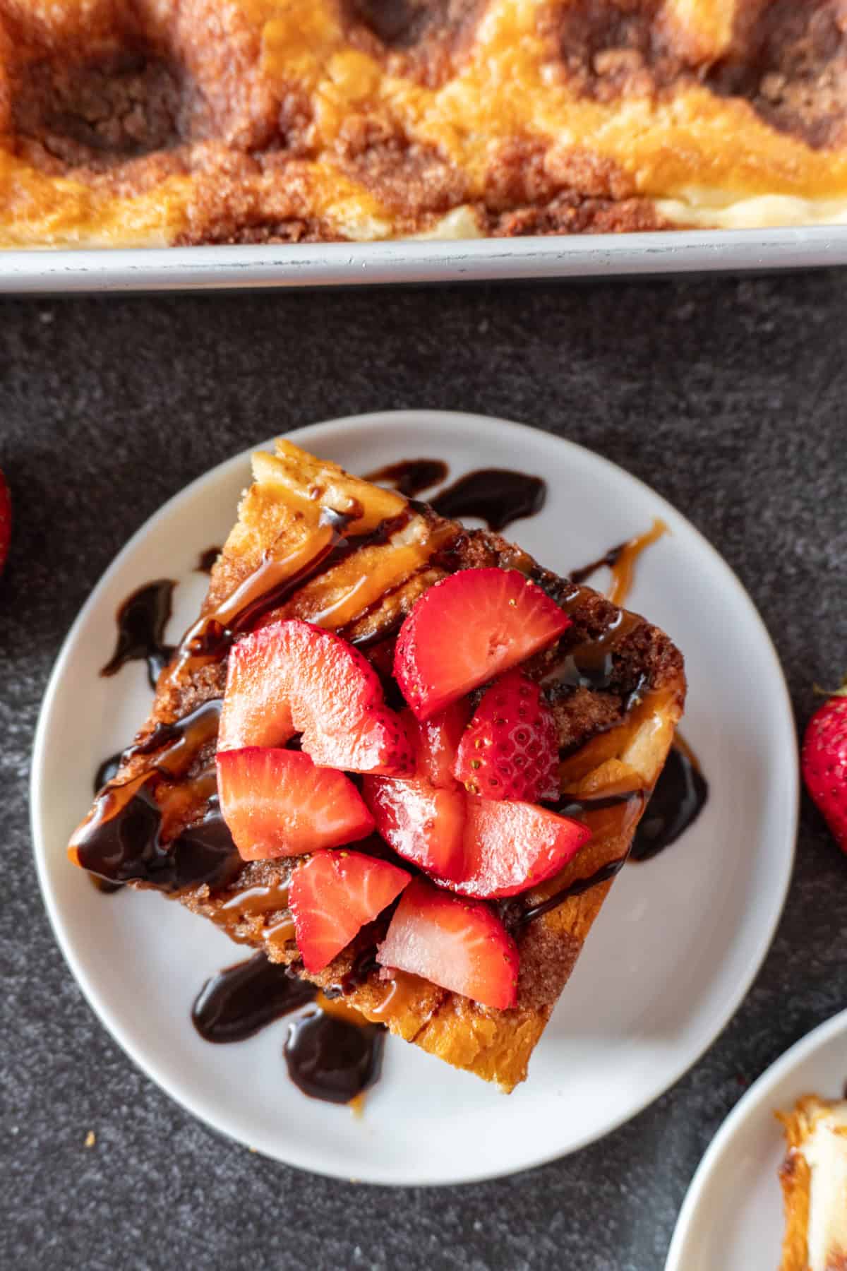 churro cheesecake bar topped with caramel sauce and chocolate sauce and strawberries on small what plate.