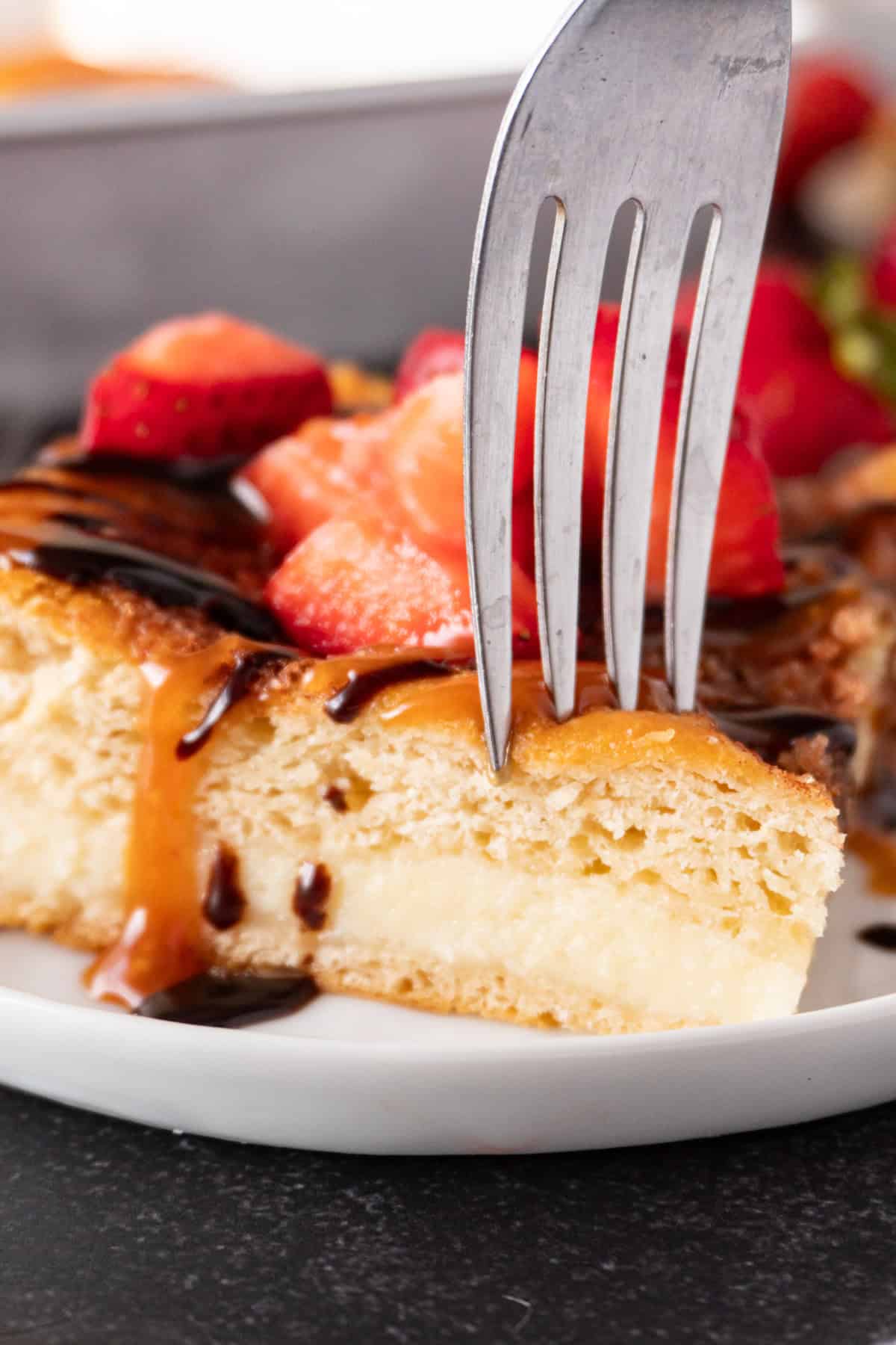 sticking a fork into churro cheesecake bar topped with caramel sauce and chocolate sauce and strawberries