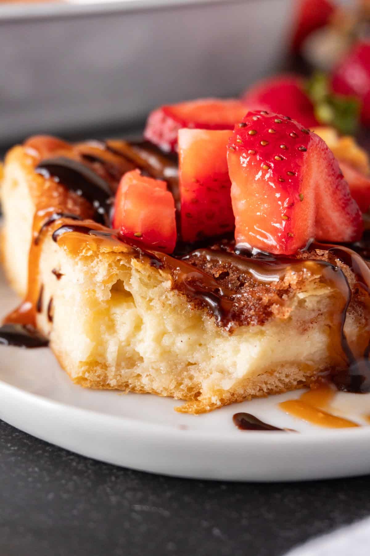 churro cheesecake bar topped with caramel sauce and chocolate sauce and strawberries on white plate.
