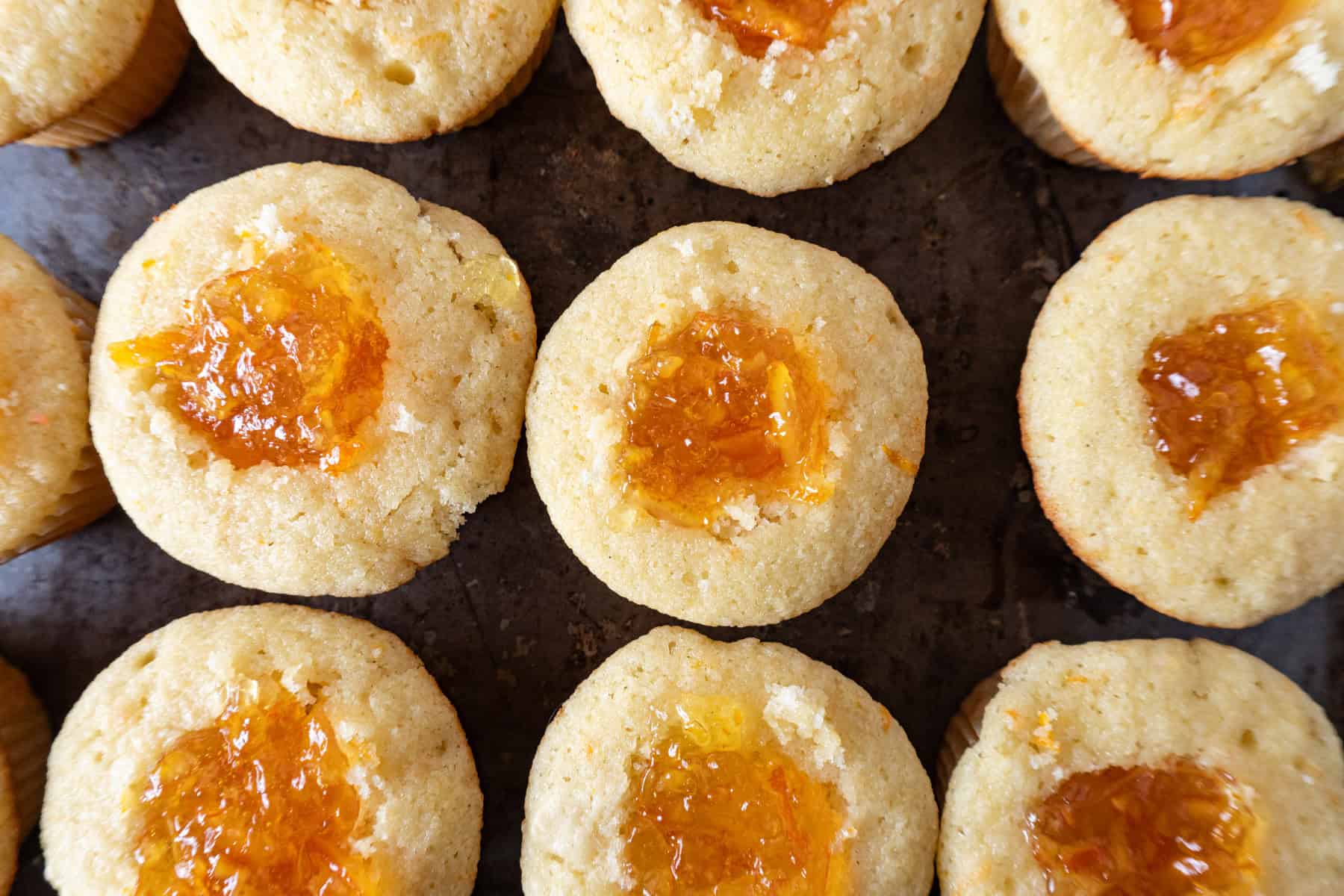 A tray of muffins with orange marmalade filling a hole in each cupcak.