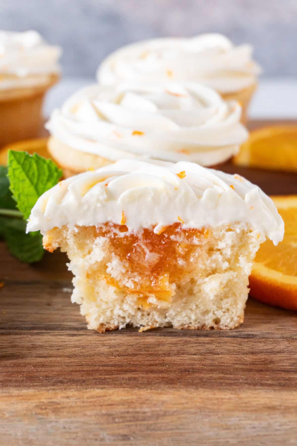 orange cupcake cut in half showing marmalade filling, sitting on wooden cutting board.